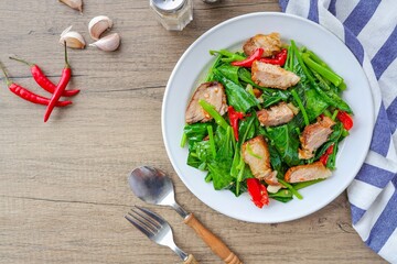 Stir fried Chinese Broccoli with crispy pork,Crispy pork with Chinese broccoli,Stir fried crispy pork in kale in a white plate on wooden background