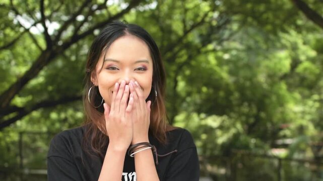 A young asian goth girl looks amazed and thrilled, mouth agape at exciting news. Pleased and ecstatic. Outdoor park scene. Slowed down 50 percent.