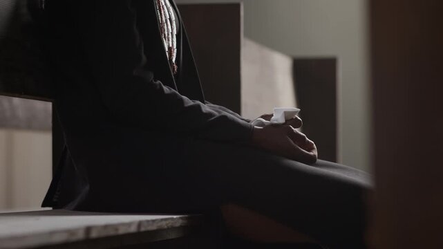 Unrecognisable man sitting on wooden pew and clutching handkerchief during prayer in church