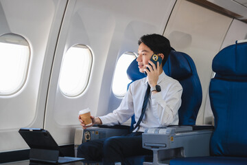 Asian man enjoying enjoys a coffee comfortable flight while sitting in the airplane cabin, Passengers near the window.