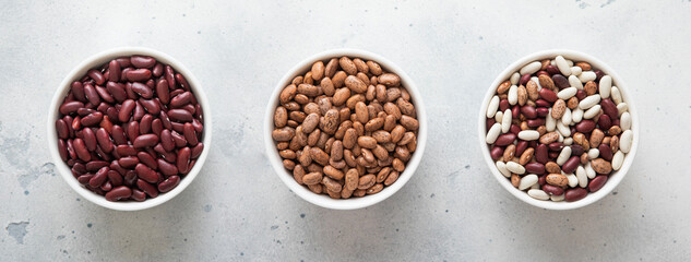 Ceramic bowls with red and variegated and mixed raw dry beans on kitchen table.Macro.
