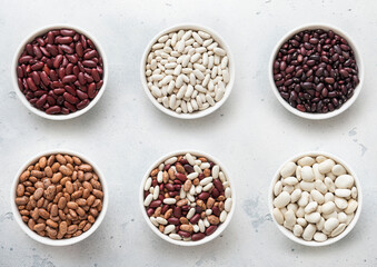 Ceramic bowls with red and white and variegated and mixed raw dry beans on kitchen table.Macro.