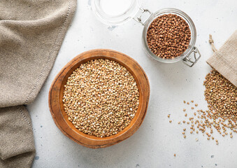 Bowl of green dry raw organic buckwheat seeds on light table with kitchen wooden spoon.Macro.