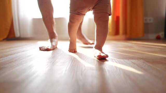 Daddy and baby taking the first steps. Child-father concept. A baby is taking the first steps on its legs. Dad teaches baby to help the little one take life his first steps in.