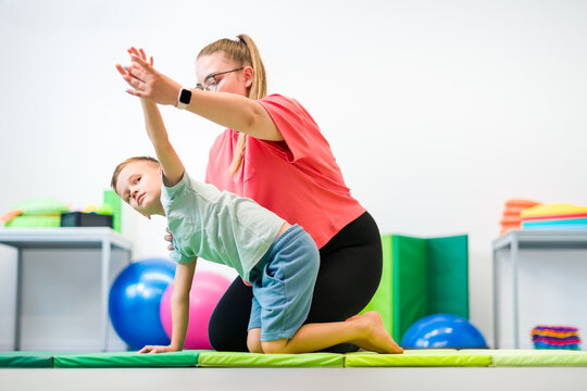 Young boy exercising with female physical therapist during therapy session. Child occupational physical therapy. Bilateral coordination.