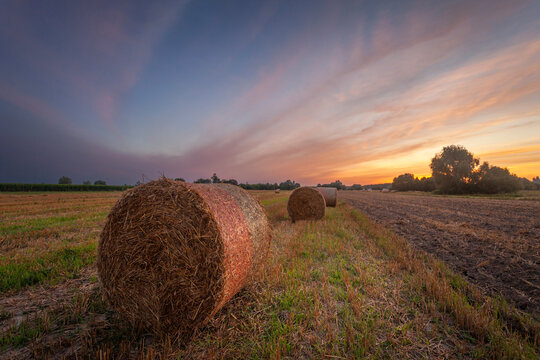 Sunset over a rural field with a bale of hay