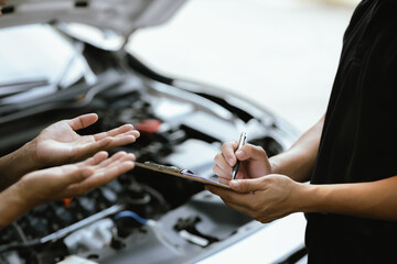 A male motor mechanic stands in a workshop, performing a safety inspection on a car engine. Surrounded by tools and equipment, he diagnoses and repairs vehicle issues.