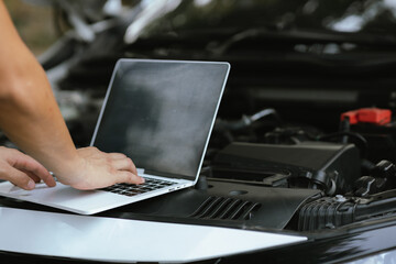 A male motor mechanic stands in a workshop, performing a safety inspection on a car engine....
