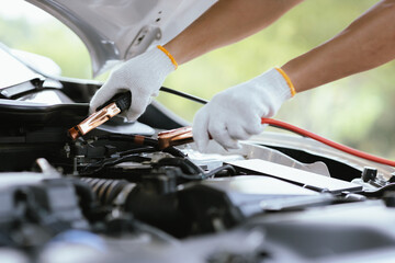 A male motor mechanic stands in a workshop, performing a safety inspection on a car engine. Surrounded by tools and equipment, he diagnoses and repairs vehicle issues.