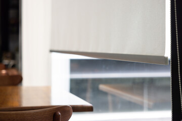 Fototapeta premium A white window shade is hanging in front of a table. white blind curtain near glass window.