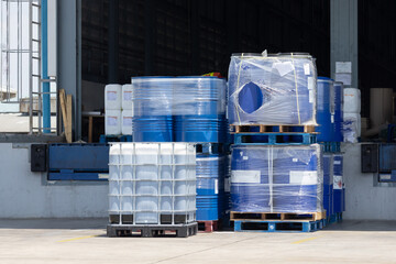 A warehouse with many barrels stacked on top of each other. white IBC contain and blue plastic tanks on wooden pallet in chemical warehouse.
