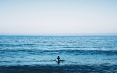 Fototapeta premium Silhouette of a Surfer on a Calm Ocean with Blue Skies.