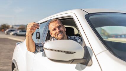 Young attractive man holding keys against white car background.