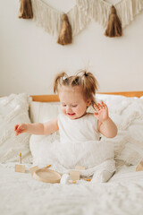 Fototapeta premium Cute beautiful girl baby sitting on the bed in the bedroom and playing in eco wooden toys cubes and pyramid