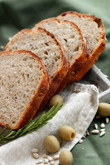 An exquisitely sliced artisan bread loaf is beautifully arranged alongside juicy tomatoes and olives on rustic fabric
