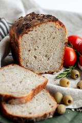 An exquisitely sliced artisan bread loaf is beautifully arranged alongside juicy tomatoes and olives on rustic fabric
