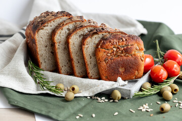 An exquisitely sliced artisan bread loaf is beautifully arranged alongside juicy tomatoes and olives on rustic fabric