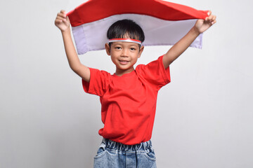 A cheerful Asian boy holding an Indonesian flag behind, isolated on white background. Indonesian Independence Day concept.