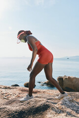A young woman in a red athletic outfit climbs rocky terrain by the sea