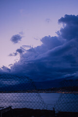 A hole in a fence leading towards the sea under dramatic purple twilight sky. A peaceful and inspiring image symbolyzing freedom, solitude, dreaming, and break from the mundane routine.