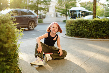 Stylish kid girl with blonde pink hairstyle pre teen age 9 -10 year old wearing trendy top and cargo pants over city street outdoor. Childhood