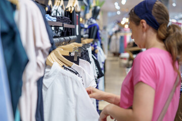 A girl looks at and chooses women's clothing in a clothing store.