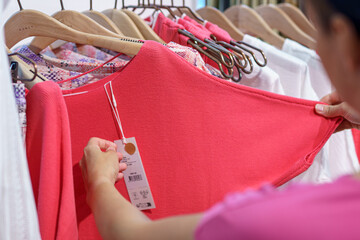 A girl looks at the price tag on women's clothes in a store.