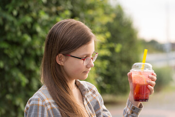 A teenage girl in glasses drinks bubble tea
