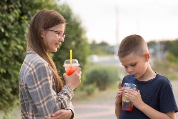 Two children drink bubble tea from plastic cups, close-up