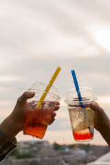 Two glasses with cold summer drink bubble tea in children's hands against the background of the sunset sky, close-up