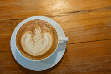 Hot latte art coffee in white ceramic cup on wooden table.