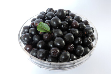 Fresh aronia berries decorated with a green leaf in a glass bowl, white background