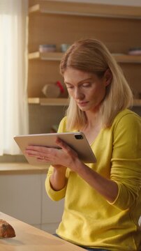 Smiling woman playing with baby while her busy wife working on tablet in kitchen