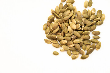A pile of pumpkin seeds (pepitas), with their characteristic flat, oval shape and greenish hue, on a white surface. A healthy and nutritious snack.