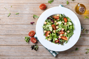 Healthy chickpea salad with tomato,lettuce and cucumber on rustic wooden table. Top view. Copy space
