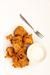Crispy, golden-brown fried chicken, likely cut into smaller pieces, served with a small white bowl of dipping sauce and a fork on a white surface. A popular and convenient meal.