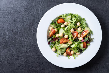 Healthy chickpea salad with tomato,lettuce and cucumber on black slate background. Top view. Copy space