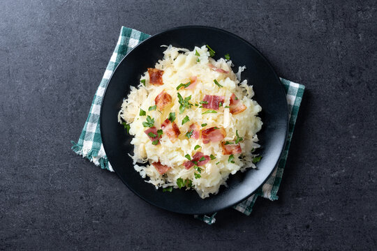 Slovak potato dumplings halusky with steamed sauerkraut and bacon on black slate background