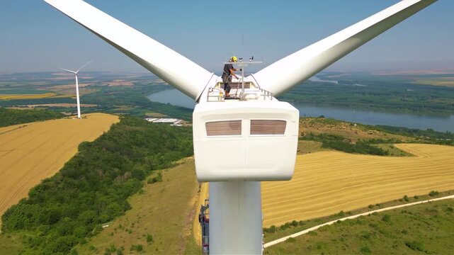 Aerial high angle footage of industrial rope access technician working on a wind turbine generator. Drone shot of skilled professional workers working at high altitude doing repairs of damaged blade.
