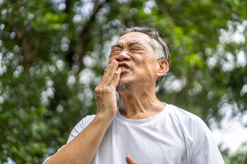 Senior asian man experiencing tooth pain, holding his cheek with pained expression, discomfort and common issues related to dental health, toothache, pain relief, and medical care for seniors at home