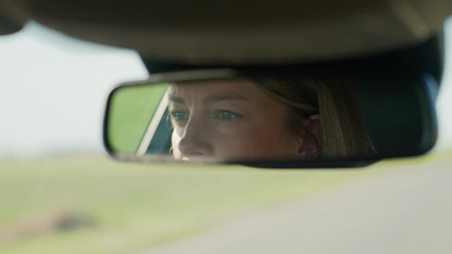 Focused woman driving car. Close up of reflection of female driver's eyes in rearview mirror. Road trip and safety driving concept