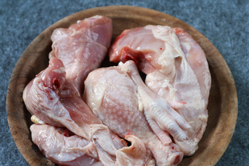 Pieces of raw chicken on a wooden plate on gray background
