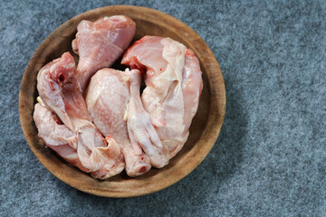 Pieces of raw chicken on a wooden plate on gray background
