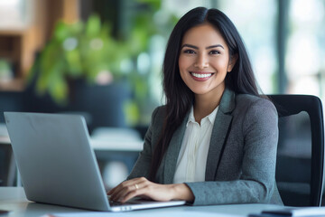 Happy latin hispanic young business woman working on laptop computer in company office. Smiling Indian entrepreneur manager businesswoman using pc for communication, learning at workplace