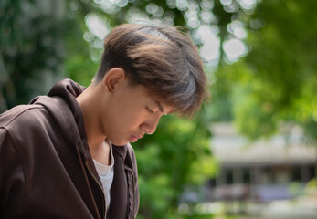 Asian teenboy in a brown shirt sits lonely in a juvenile detention community center, awaiting further release, depression,freedom and detention of young people concept.