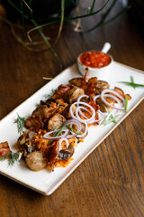 Delicious, juicy shashlik with fresh vegetables, fragrant herbs, and adjika sauce, served on a beautiful white plate on a wooden table in a cozy, charming setting