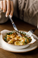 cute girl is enjoying a delicious dish with crispy potatoes, fresh vegetables, fragrant herbs, and creamy cheese on a beautiful black plate in a cozy, charming café.