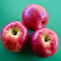 Three Pink Lady apples against a green background.