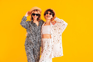 Two young beautiful smiling brunette hipster female in trendy summer clothes. Sexy women posing near yellow wall in studio. Positive models having fun. Cheerful and happy