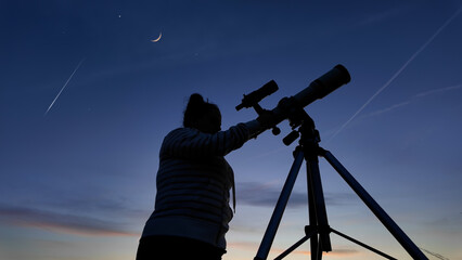 Amateur astronomer looking at the evening skies, observing planets, stars, Moon and other celestial objects with a telescope.